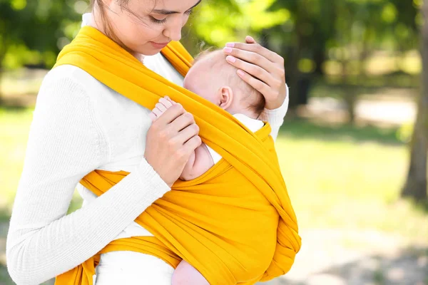 Giovane madre con il suo bambino in fionda passeggiando nel parco — Foto Stock