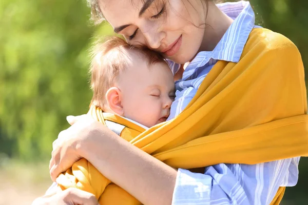 Giovane madre con il suo bambino in fionda passeggiando nel parco — Foto Stock