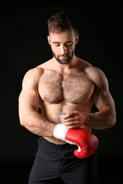 Boxeador masculino fuerte que se pone guantes contra el fondo oscuro — Foto de Stock