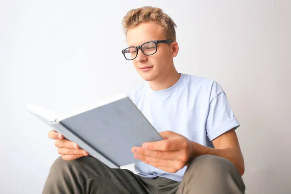 Estudiante masculino leyendo libro mientras se prepara para el examen en fondo claro — Foto de Stock