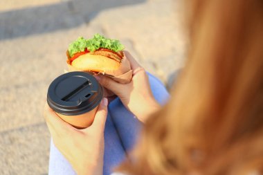 Lezzetli burger ve kahve fincan açık havada, closeup ile güzel genç kadın