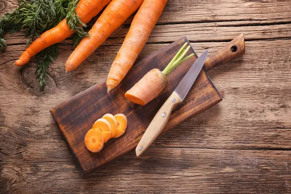 Cutting board with fresh carrot on wooden background — Stock Photo, Image