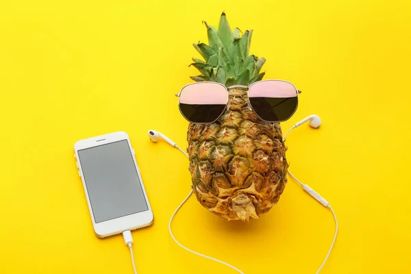 Stock image Funny pineapple with sunglasses, mobile phone and earphones on color background