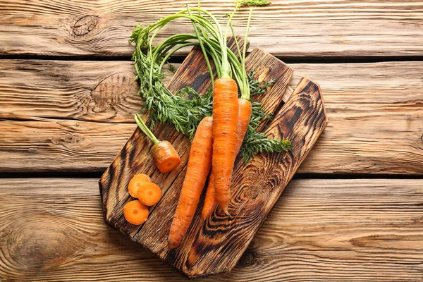 Board with fresh carrot on wooden background — Stock Photo, Image