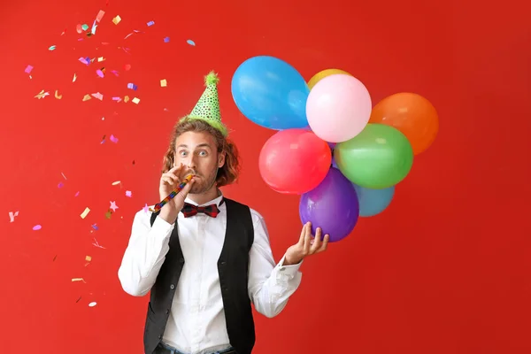 Doğum günü balonları ve renk arka plan üzerinde parti düdük ile genç adam — Stok fotoğraf