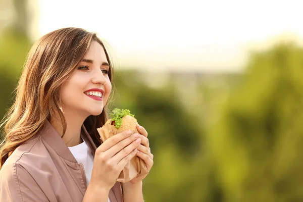 Piękna młoda kobieta z pysznym Burger na świeżym powietrzu — Zdjęcie stockowe