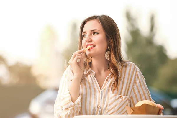 Beautiful young woman eating tasty french fries in outdoor cafe — Stock Photo, Image