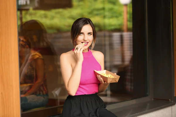 Schöne junge Frau isst leckere Pommes in Outdoor-Café — Stockfoto