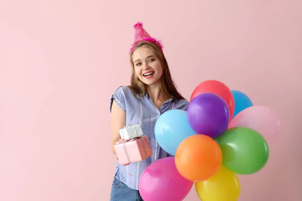 Mujer feliz con regalos y globos de cumpleaños en el fondo de color — Foto de Stock