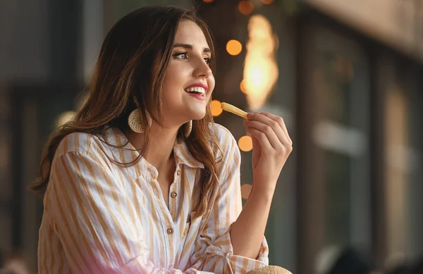 Beautiful young woman eating tasty french fries outdoors — Stock Photo, Image