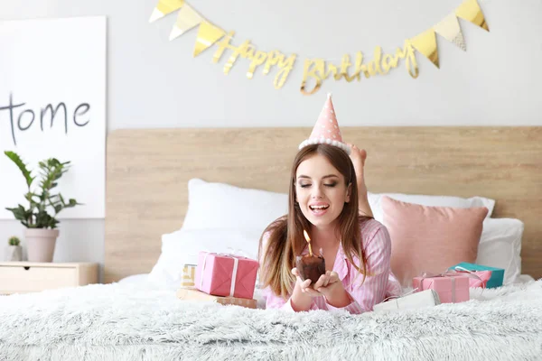 Mujer feliz con pastel de cumpleaños acostado en la cama en casa — Foto de Stock