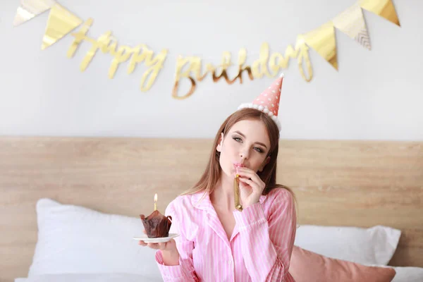 Szczęśliwa kobieta z tort urodzinowy i gwizdek party w sypialni w domu — Zdjęcie stockowe