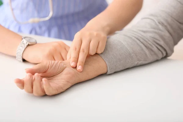 Young doctor checking pulse of elderly woman in clinic — Stock Photo, Image