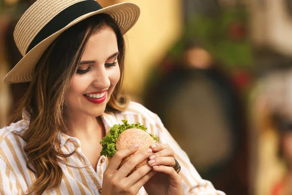 Красивая молодая женщина ест вкусный бургер на открытом воздухе — стоковое фото