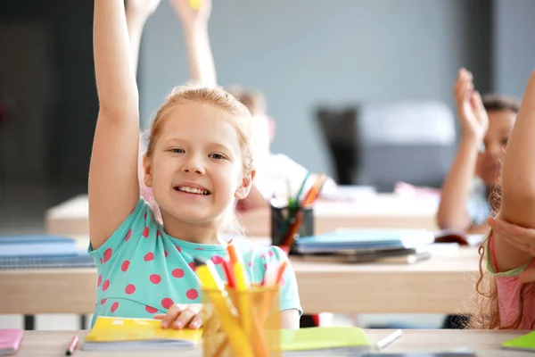 Schattig klein meisje verhogen hand tijdens les in klaslokaal — Stockfoto