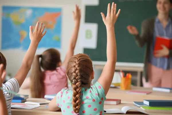 Schattige kleine leerlingen die de handen opsteken tijdens een les in het klaslokaal — Stockfoto