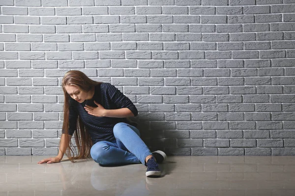 У женщины приступ паники, когда она сидит у кирпичной стены — стоковое фото