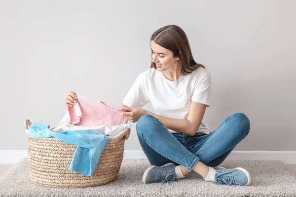 Beautiful young woman with laundry sitting on floor near white wall — Stock Photo, Image