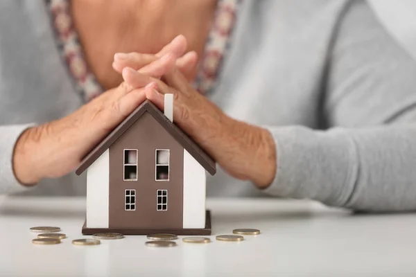 Ältere Frau mit Hausfigur und Münzen, Nahaufnahme. Konzept der Bezahlung für Versorgungsleistungen — Stockfoto