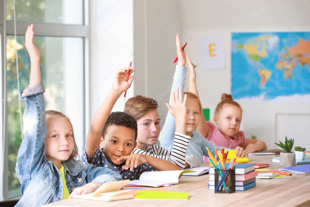 Cute little pupils raising hands during lesson in classroom