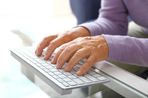 Elderly woman using modern computer keyboard at table, closeup