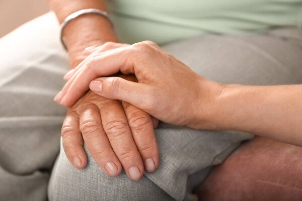 Young daughter supporting elderly mother at home, closeup