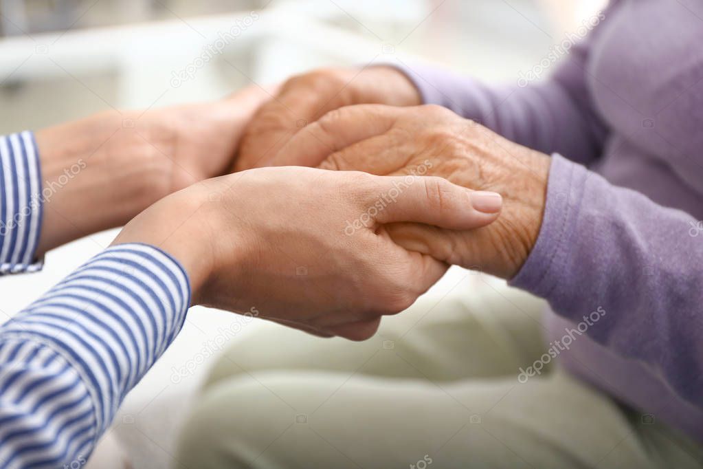 Young daughter supporting elderly mother at home, closeup