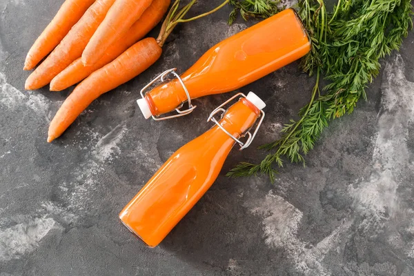 Bottles of tasty carrot juice on grunge background — Stock Photo, Image