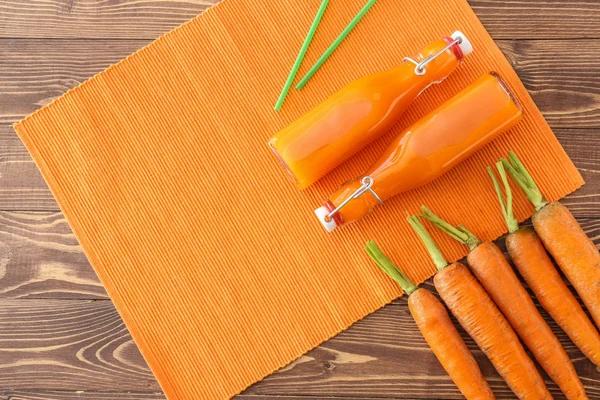 Bottles of tasty carrot juice on wooden table — Stock Photo, Image