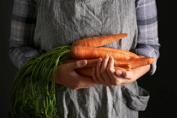 Woman holding fresh carrots on dark background, closeup — Stock Photo, Image