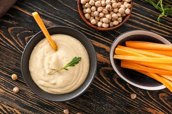 Bowl of tasty sauce and fresh carrot on wooden table — Stock Photo, Image