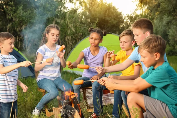 Group of children cooking sausages on campfire