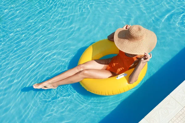 Beautiful young woman relaxing on inflatable ring in swimming pool — Stock Photo, Image