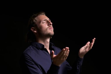 Dindar genç adam karanlık arka planda dua ediyor.