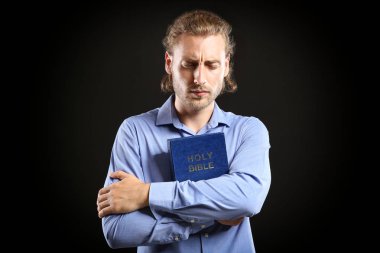 Dindar genç adam karanlık arka planda dua ediyor.