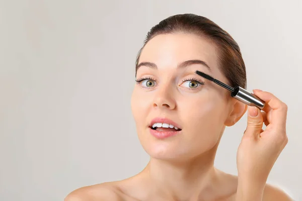 Vacker ung kvinna med ögonfransförlängning tillämpa mascara mot grå bakgrund — Stockfoto