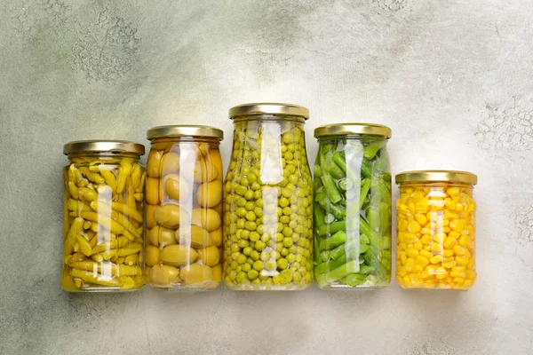 Баночки з різними консервованими овочами та бобовими на світлому фоні — стокове фото