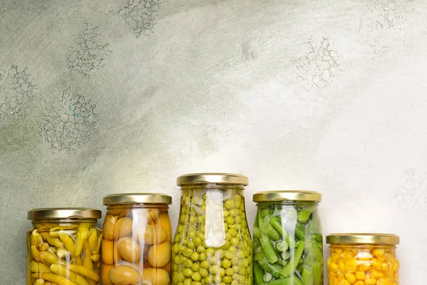 Jars with different canned vegetables and legumes on light background — Stock Photo, Image