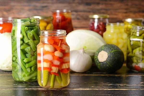 Frascos com diferentes vegetais enlatados na mesa de madeira — Fotografia de Stock