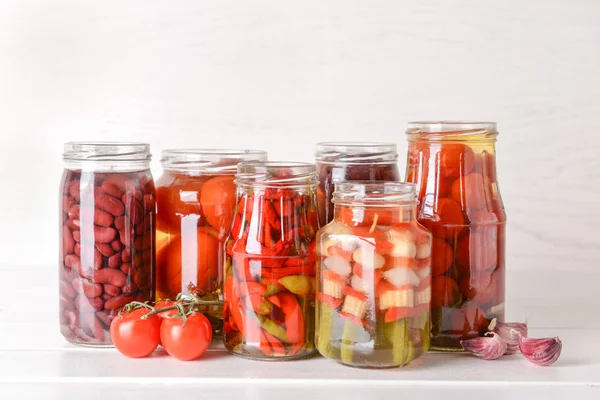 Frascos con diferentes verduras enlatadas y frijoles sobre mesa blanca —  Fotos de Stock