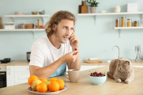 Man talking by phone while sitting at kitchen table with cute funny cat — Stock Photo, Image