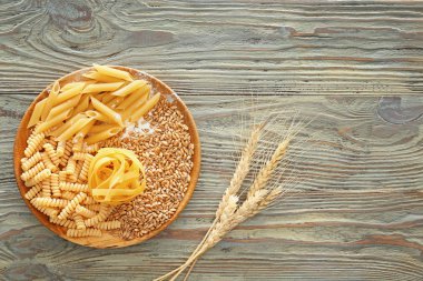 Ahşap masa üzerinde kuru makarna ve buğday taneleri ile plaka