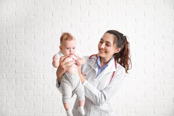 Pediatrician with cute little baby against white brick wall — Stock Photo, Image