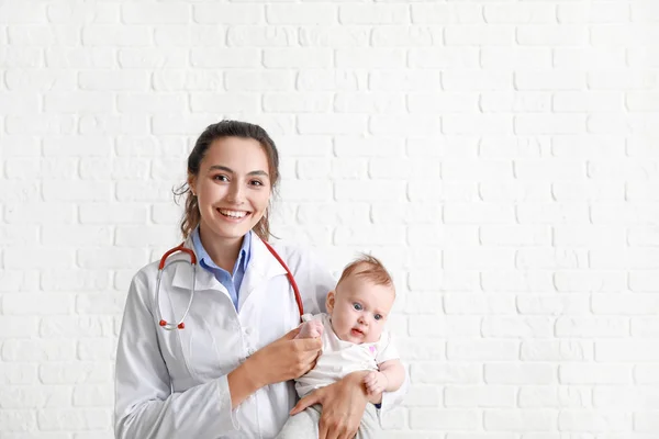 Pediatrician with cute little baby against white brick wall — Stock Photo, Image