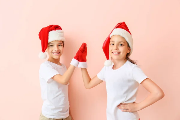 Glückliche kleine Kinder in Weihnachtsmützen, die einander vor farbigem Hintergrund High-Five geben — Stockfoto