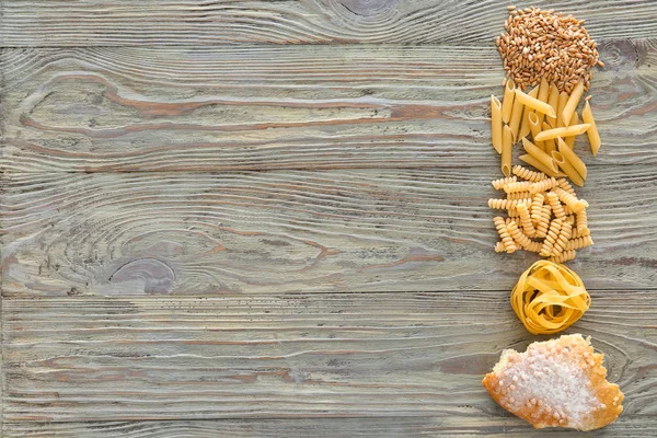 Tarwekorrels met droge pasta en een stukje brood op houten achtergrond — Stockfoto