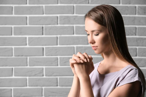 Vallásos fiatal nő, aki a téglafal ellen imádkozik — Stock Fotó