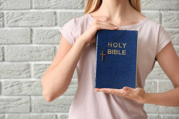 Religiös ung kvinna med bibel mot tegelvägg — Stockfoto