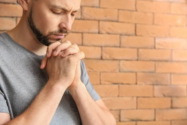 Religious man praying against brick wall — Stock Photo, Image