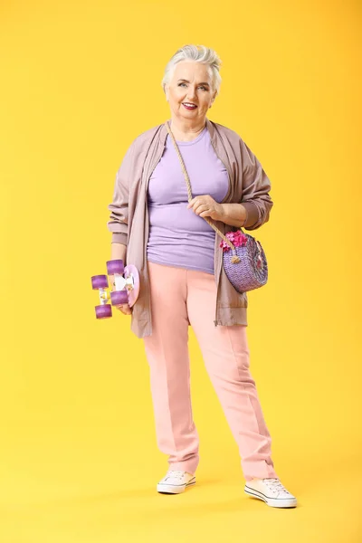 Stylish elderly woman with skateboard on color background — Stock Photo, Image